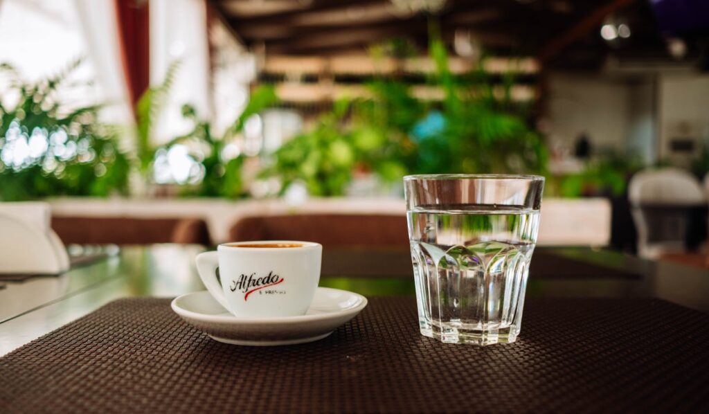 Espresso cup and water glass on a café table with lush greenery background in Sochi, Russia.